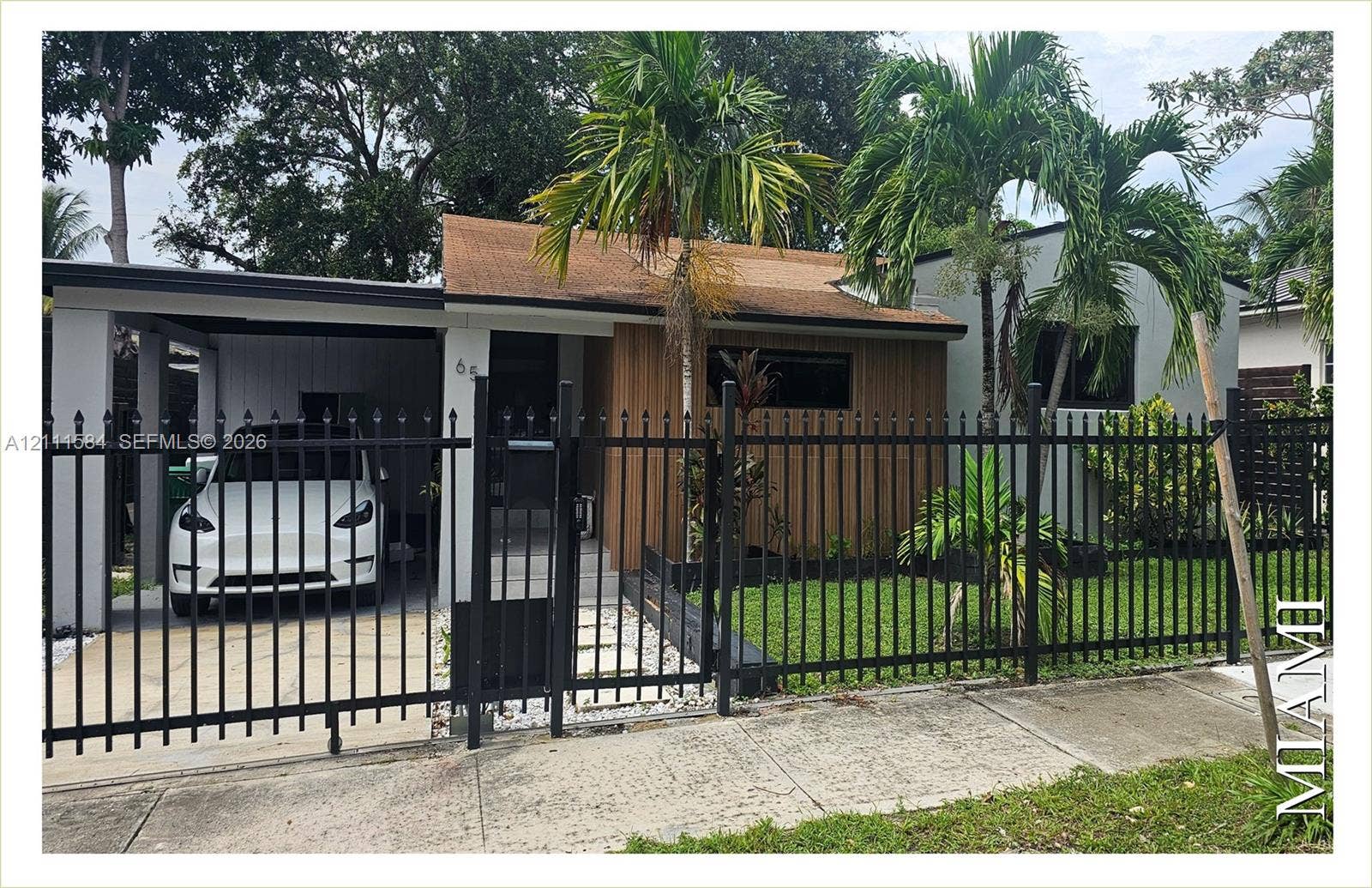 Exterior facade featuring wood-finish siding, metal perimeter fencing, a covered carport, and concrete paver walkway