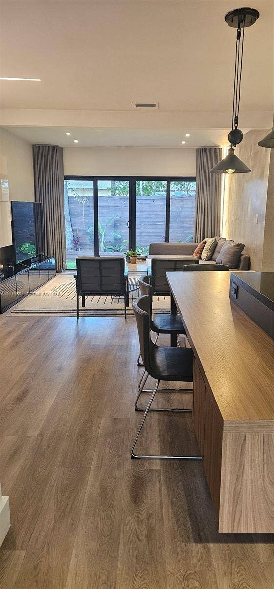 Open-concept interior featuring wood-finish flooring, recessed lighting, a built-in kitchen island, and multi-panel glass doors leading to the exterior