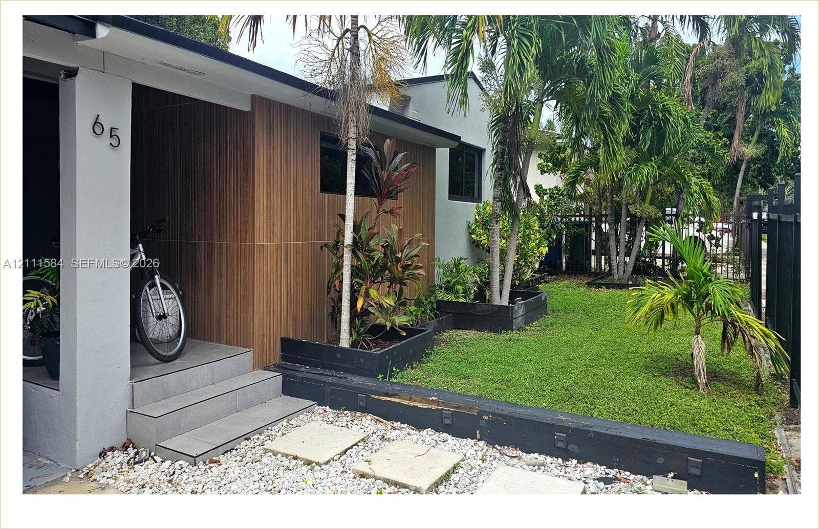 Exterior facade featuring wood-panel siding, tiled entryway steps, integrated garden beds, and manicured turf