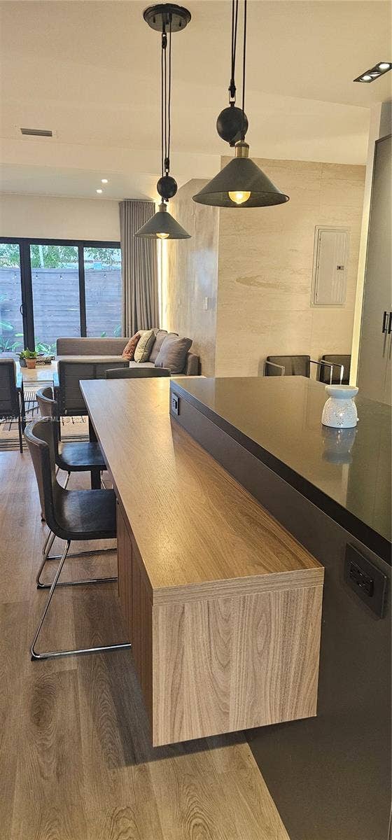 Kitchen island featuring a dual-level design with a wood-finish counter and dark countertop, complemented by two adjustable pendant lights and wood-finish flooring