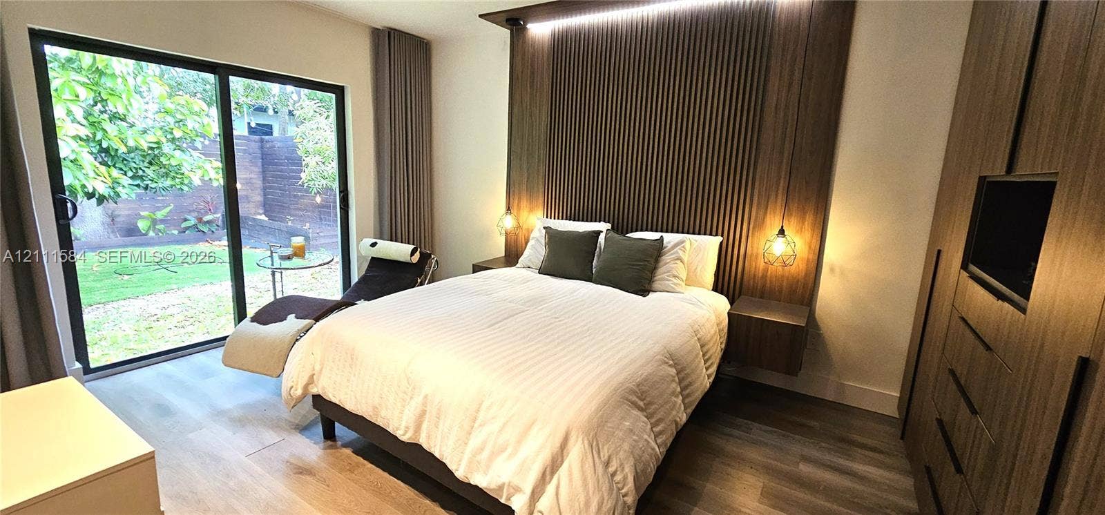 Sliding glass door leading to exterior, custom vertical wood-slat accent wall, integrated floating nightstands, and built-in wood-finish cabinetry