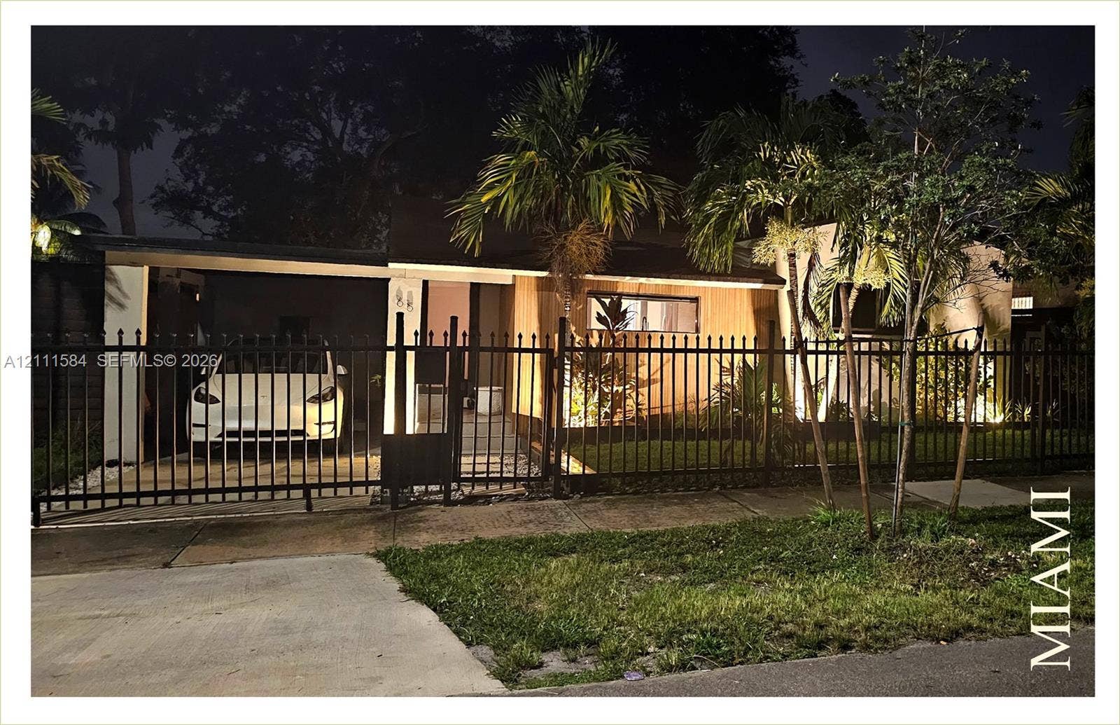 Single-story exterior featuring wood-tone paneling, a concrete carport, and a metal perimeter fence with a gate