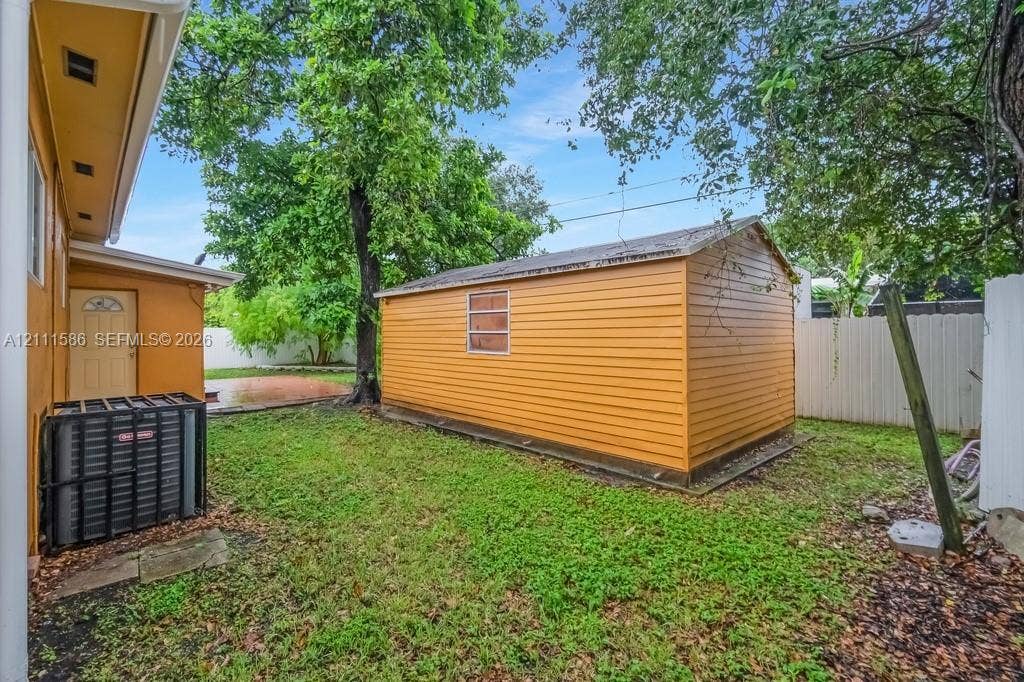 20431 NE 14th Court, Miami, FL 33179 Backyard area featuring a detached storage structure with horizontal siding, a fenced perimeter, and mature trees