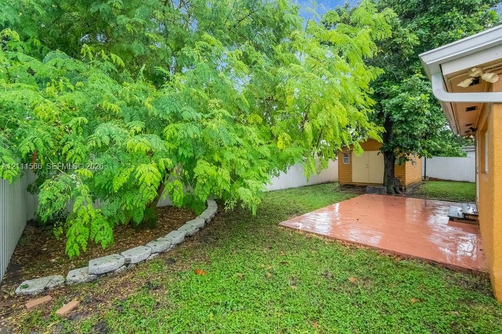 20431 NE 14th Court, Miami, FL 33179 Rear yard featuring a paved patio, detached storage structure, stone garden edging, and mature trees enclosed by privacy fencing