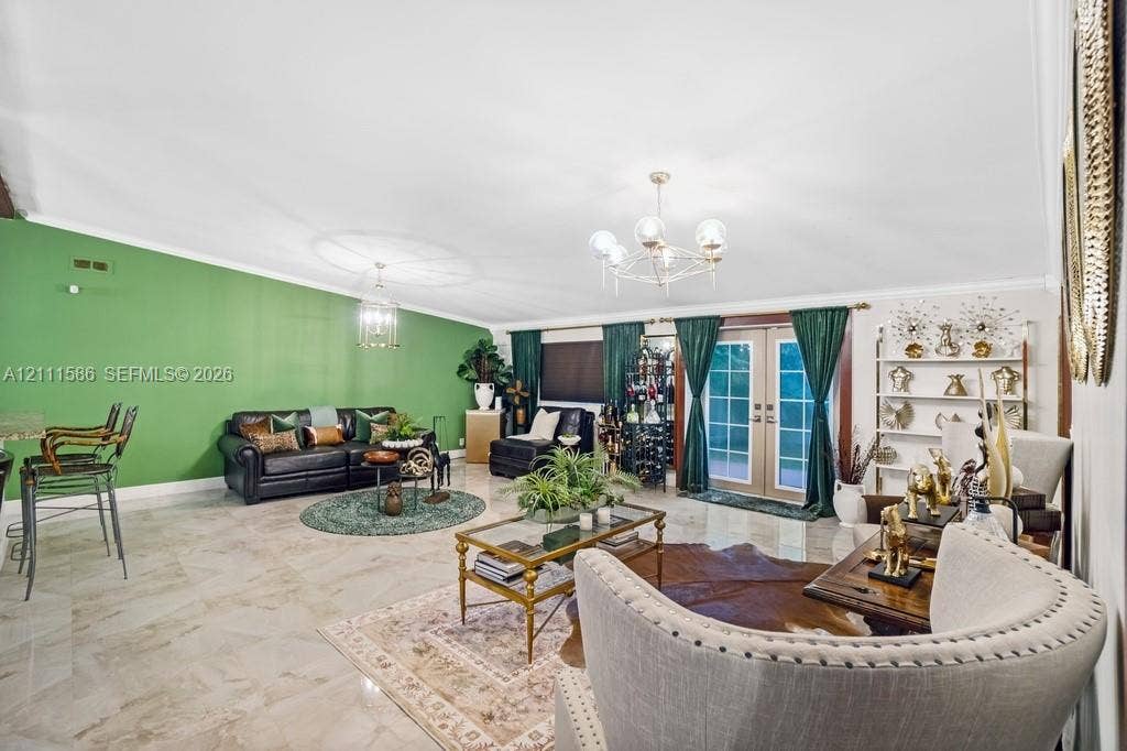 20431 NE 14th Court, Miami, FL 33179 Open-concept living space featuring high vaulted ceilings, light-toned stone-finish flooring, a multi-arm polished metal chandelier, and full-height glass-paneled double doors