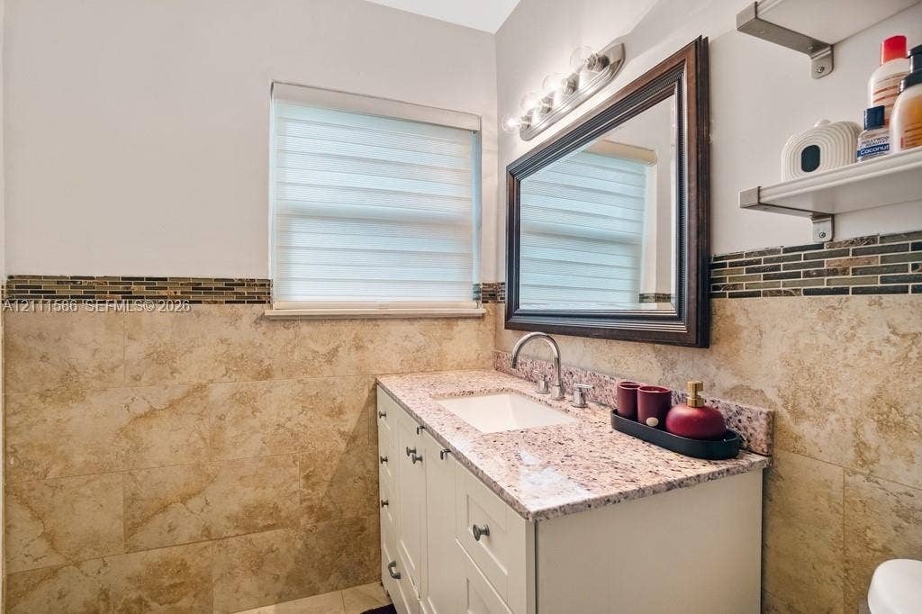 20431 NE 14th Court, Miami, FL 33179 Bathroom vanity with stone countertop, undermount sink, multi-drawer white cabinetry, framed wall mirror, and decorative tile wainscoting