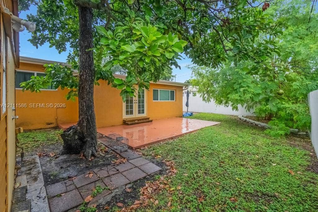 20431 NE 14th Court, Miami, FL 33179 Rear exterior featuring a concrete patio, French doors, mature tree, stone-tile walkway, and privacy fencing