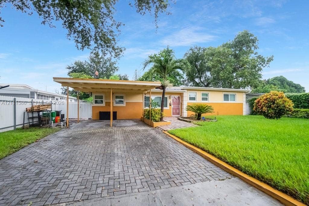 20431 NE 14th Court, Miami, FL 33179 Single-story exterior featuring an attached carport, herringbone-patterned paved driveway, front lawn, and vinyl privacy fencing