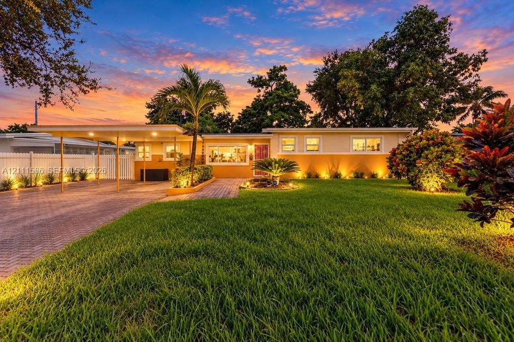 20431 NE 14th Court, Miami, FL 33179 Single-story exterior featuring a paved brick driveway, attached carport, white privacy fencing, and professional landscaping