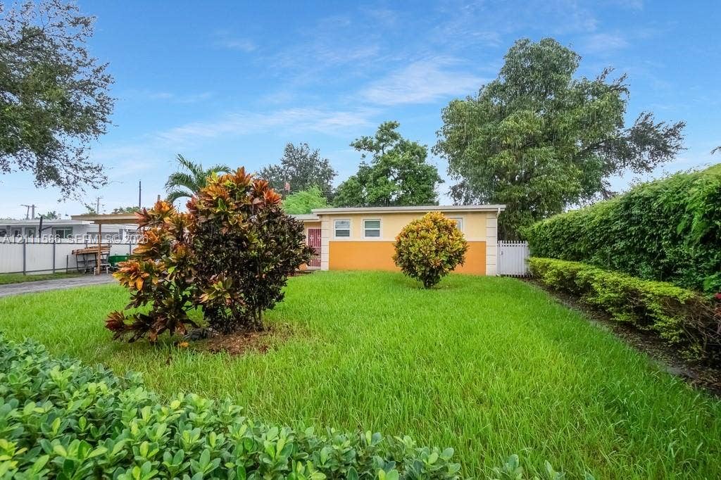 20431 NE 14th Court, Miami, FL 33179 Exterior view featuring a fenced yard with manicured lawn, established shrubbery, and a private side gate