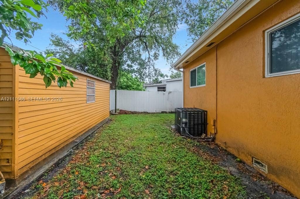 20431 NE 14th Court, Miami, FL 33179 Exterior side yard featuring a stucco-finish wall, horizontal-siding storage structure, and vinyl privacy fencing