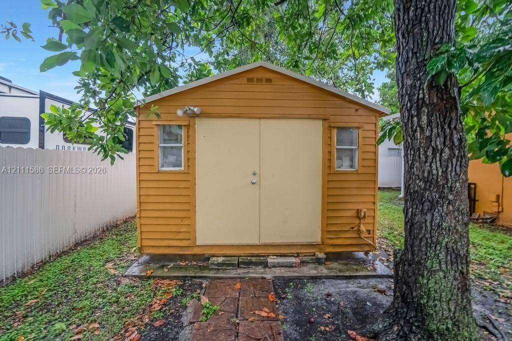 20431 NE 14th Court, Miami, FL 33179 Detached storage shed featuring horizontal lap siding, double doors, dual windows, and an exterior light fixture, set on a stone paver path