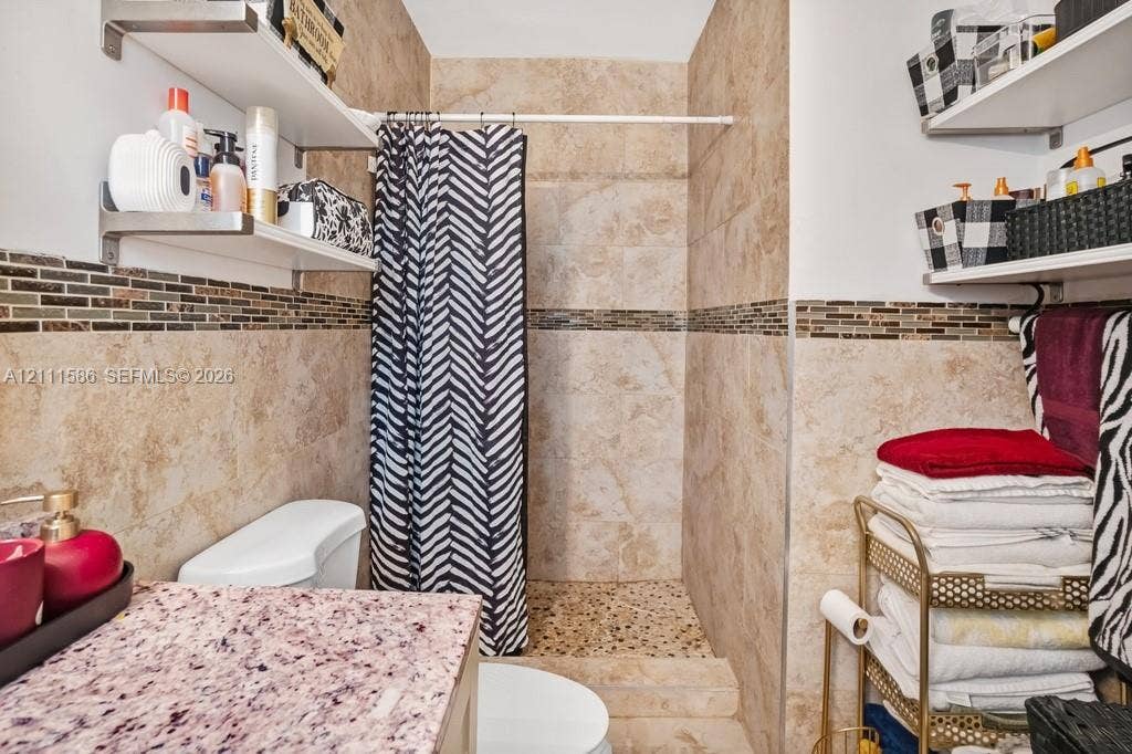 20431 NE 14th Court, Miami, FL 33179 Bathroom featuring large-format tile wall cladding, glass and stone mosaic tile accents, a walk-in shower with pebble-stone flooring, and floating wall-mounted shelving