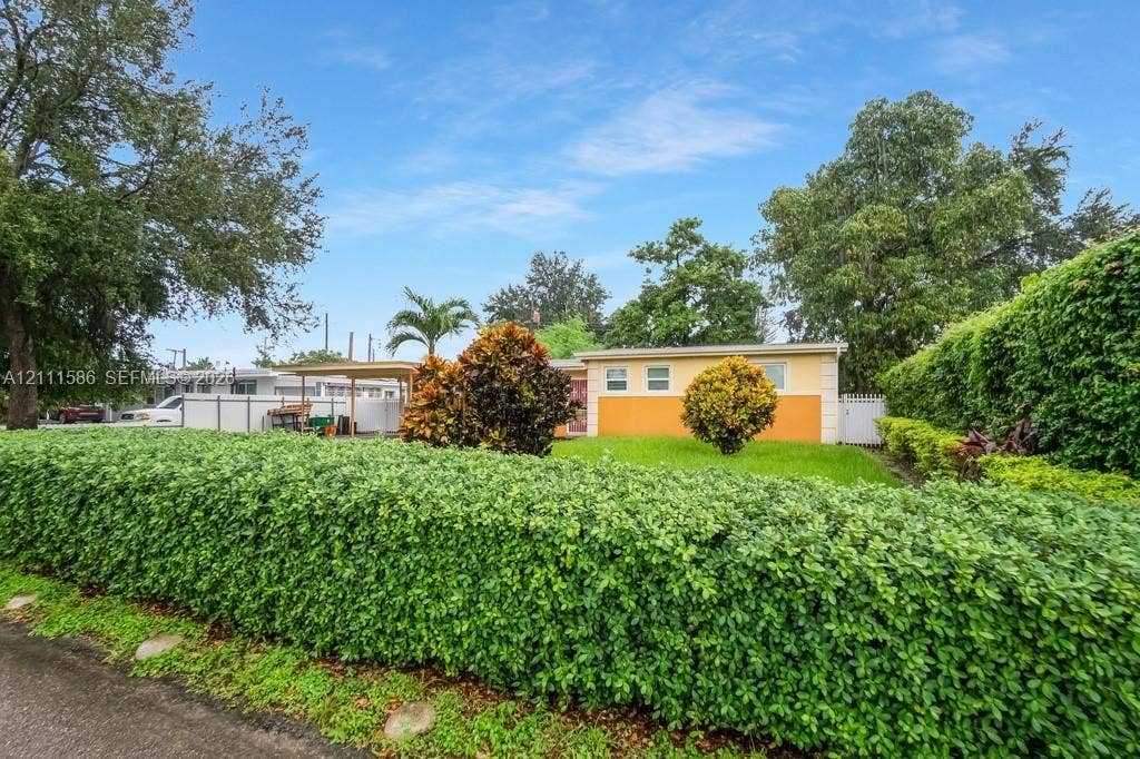 20431 NE 14th Court, Miami, FL 33179 Exterior facade featuring a two-tone stucco finish, expansive manicured lawn, established perimeter hedge, and integrated carport