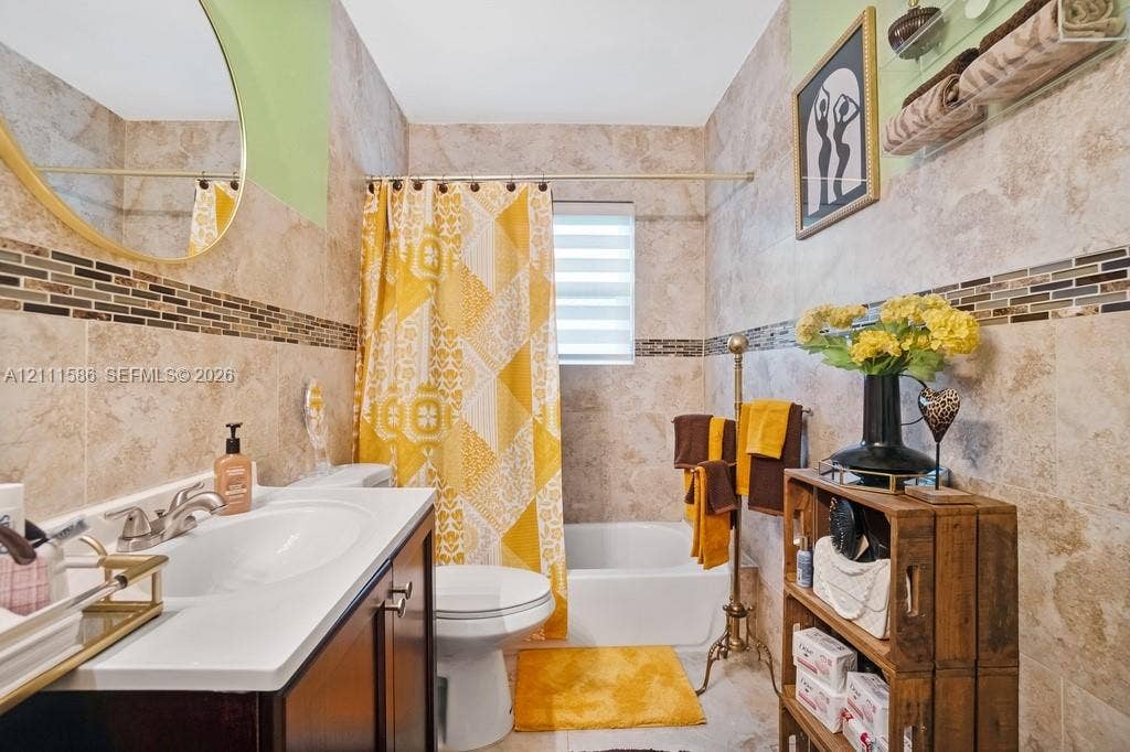 20431 NE 14th Court, Miami, FL 33179 Full-wall tile surround featuring decorative mosaic accent tiling, vanity with an integrated white sink, circular mirror with metallic frame, and tiered horizontal blind