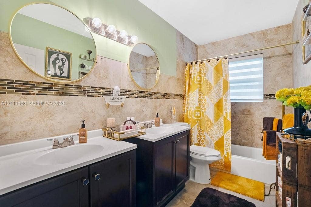 20431 NE 14th Court, Miami, FL 33179 Dual dark-finish vanities with integrated sinks, large round wall-mounted mirrors, and tiled shower surround with decorative mosaic accent inlay