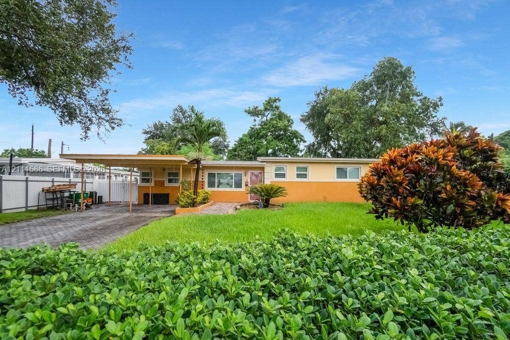 20431 NE 14th Court, Miami, FL 33179 Single-story residence featuring a two-tone exterior, attached carport, paver driveway, manicured lawn, and privacy fencing