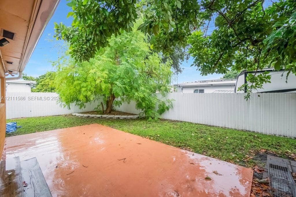 20431 NE 14th Court, Miami, FL 33179 Rear exterior space featuring a concrete patio, perimeter vinyl fencing, and a mature tree within a landscaped garden bed