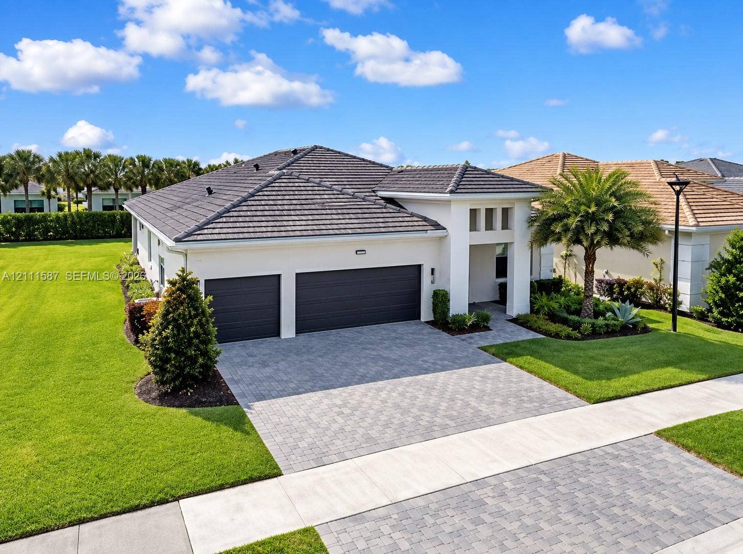 Single-story residence featuring a concrete tile roof, a three-car garage, and a paver driveway