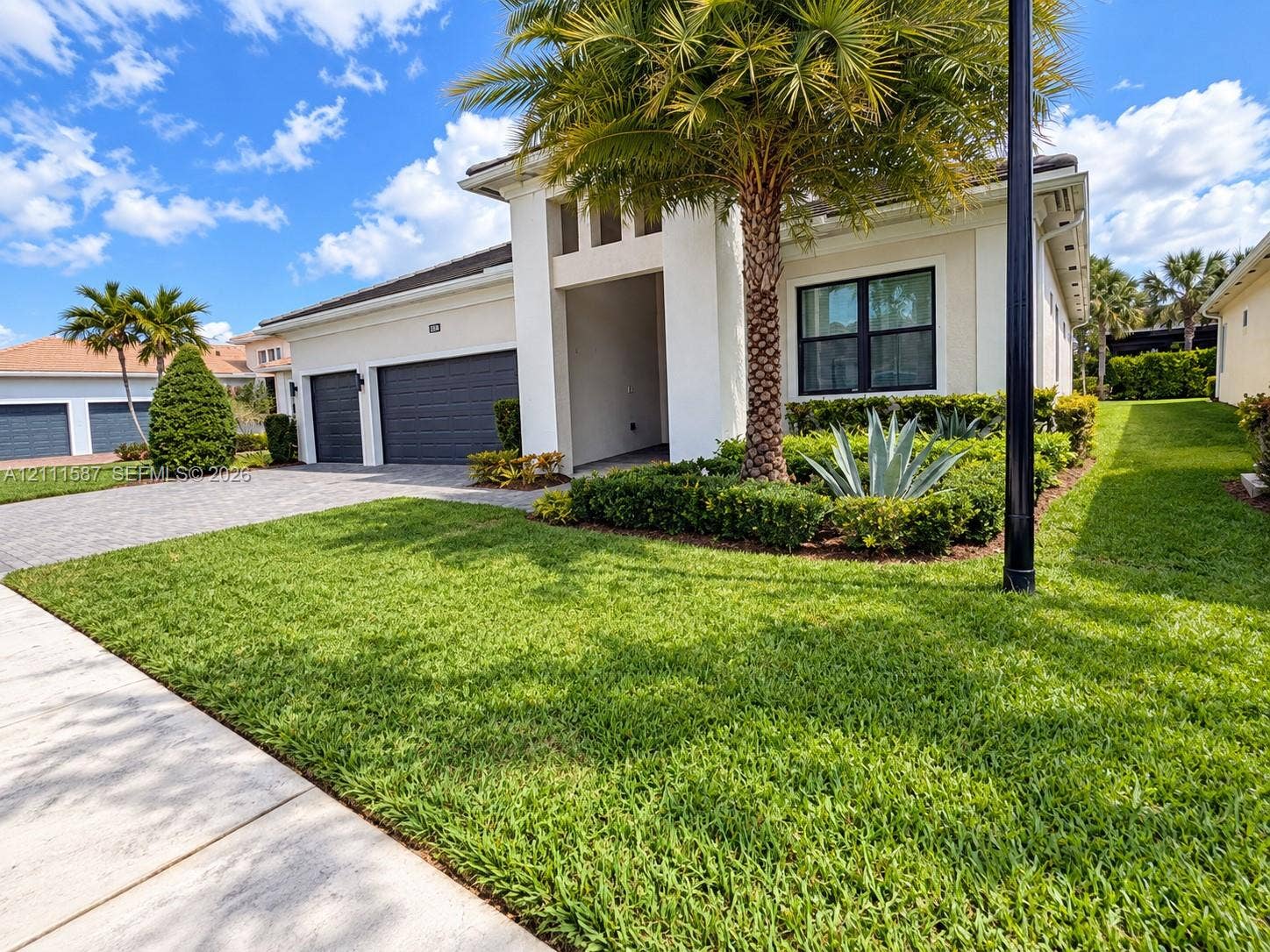 Single-story exterior featuring a paver driveway, three-car garage, recessed entryway, and manicured landscaping