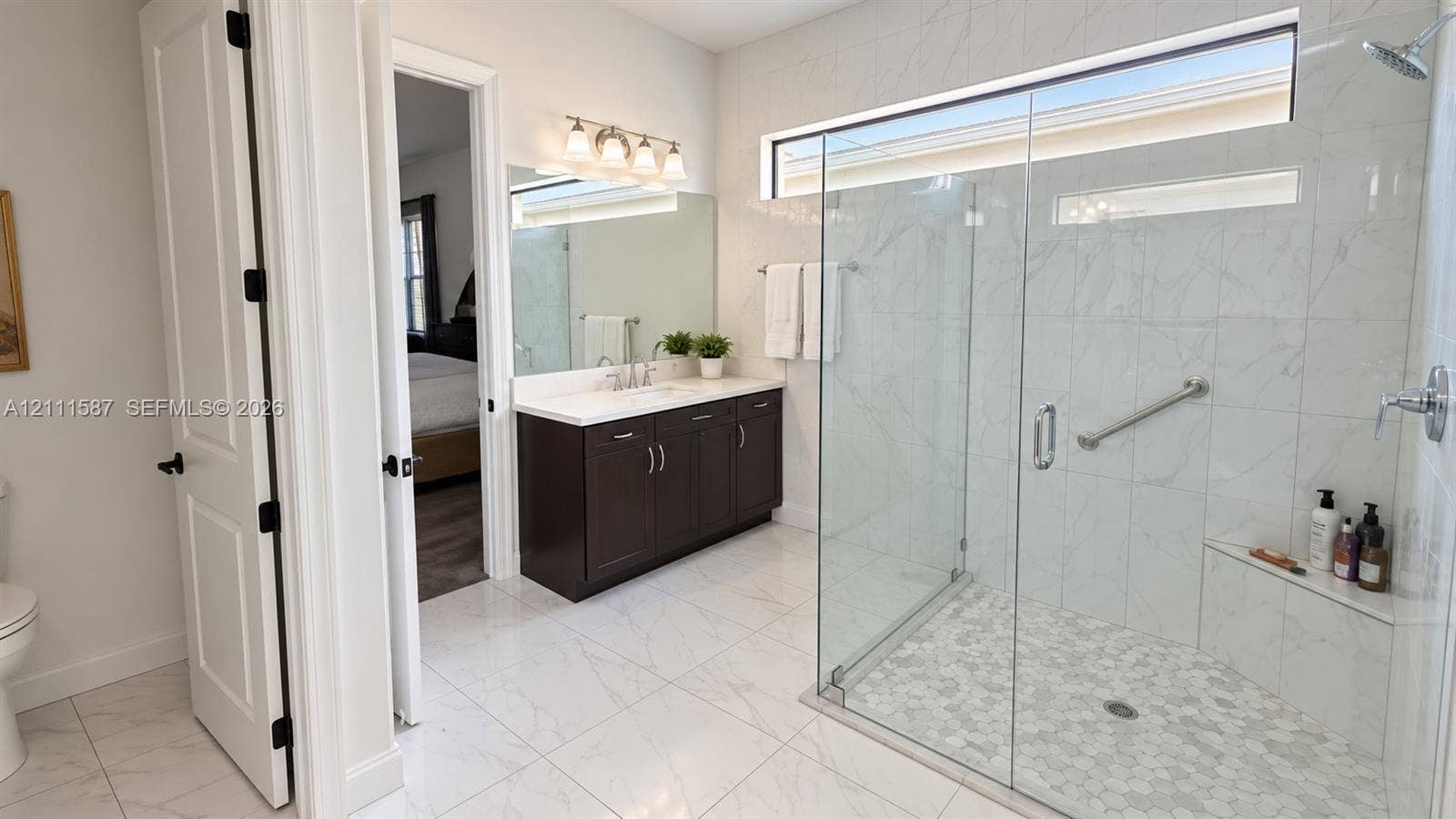 Walk-in shower with stone-finish tile surround, frameless glass enclosure, and built-in bench seating, complemented by a dark wood vanity with white countertop and large vanity mirror