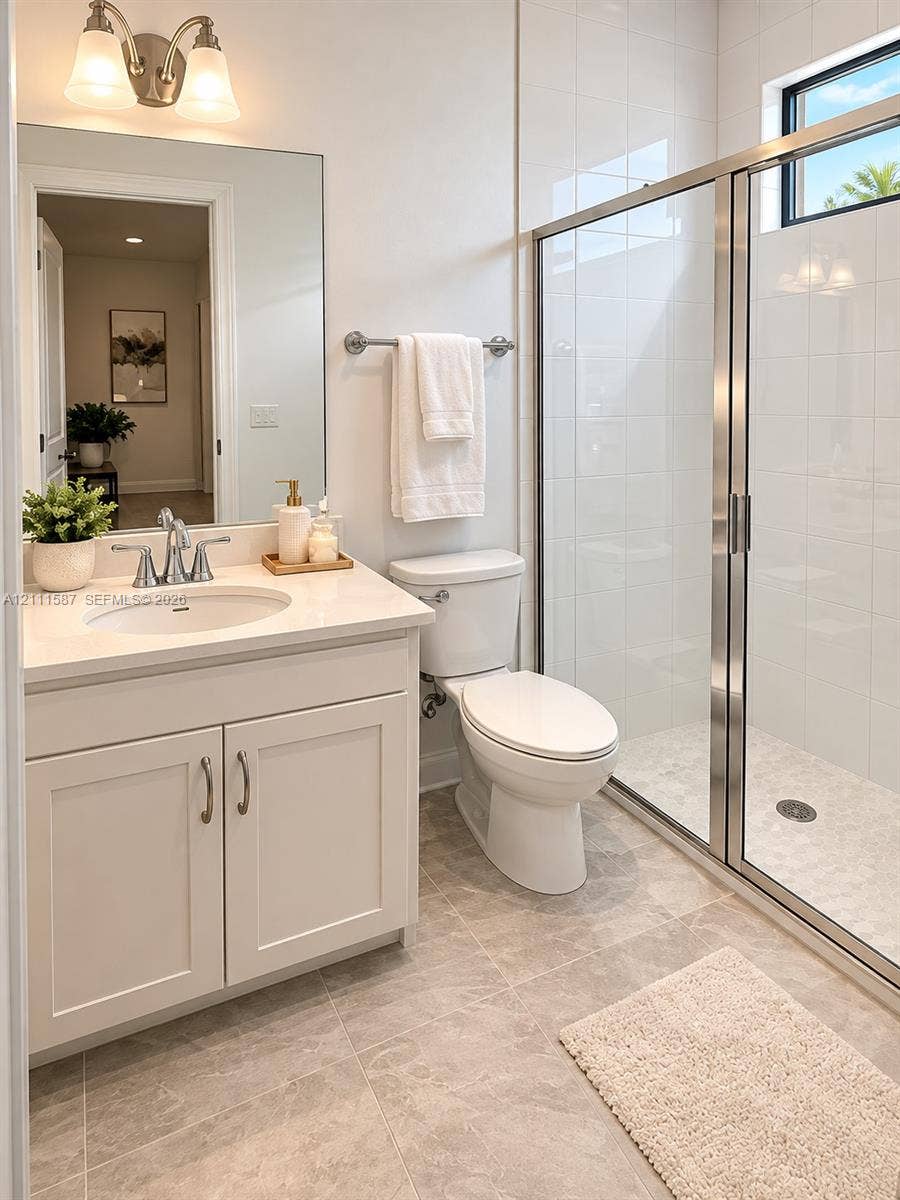 Bathroom featuring a vanity with a light-toned countertop, integrated basin, and brushed-nickel faucet, accompanied by a walk-in shower with floor-to-ceiling tile surround and metal-framed glass enclosure, complemented by large-format neutral-tone tile flooring