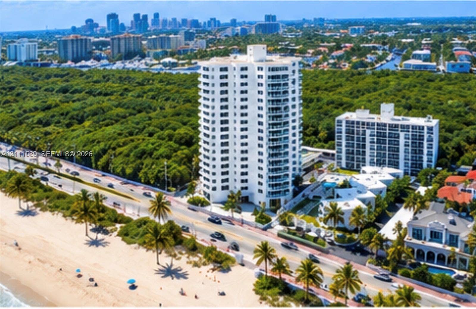 High-rise residential tower featuring a white facade, private balconies, an attached swimming pool, landscaped grounds, and immediate proximity to the coastline