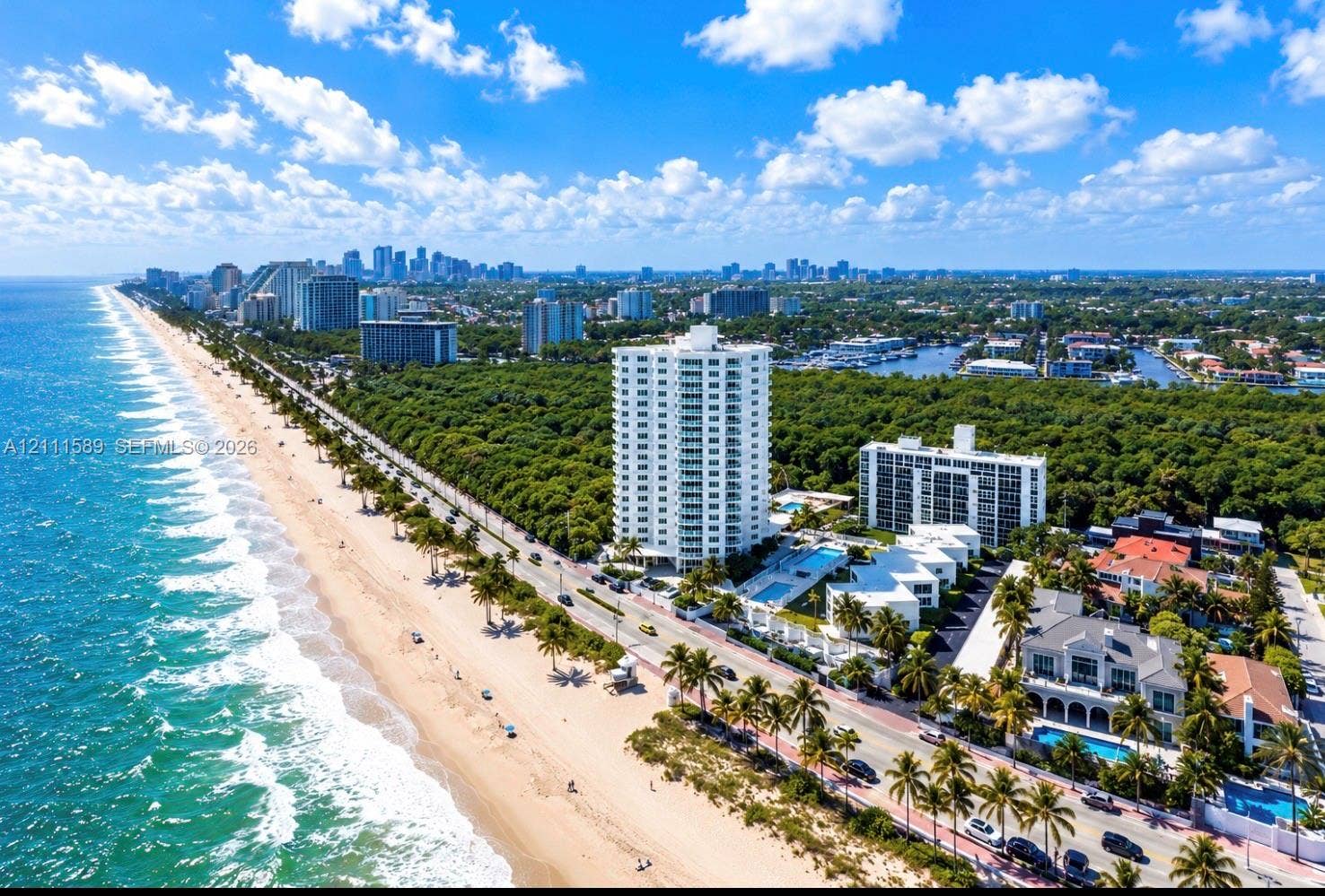 Aerial perspective of oceanfront high-rise building with direct proximity to sandy beach, perimeter landscaping, and established coastal vegetation