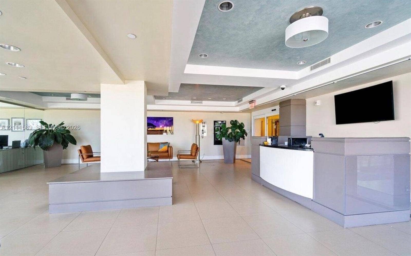 Reception area featuring large-format tile flooring, a tiered tray ceiling with recessed lighting, a structured built-in service counter, and an integrated central pillar with a stepped platform base