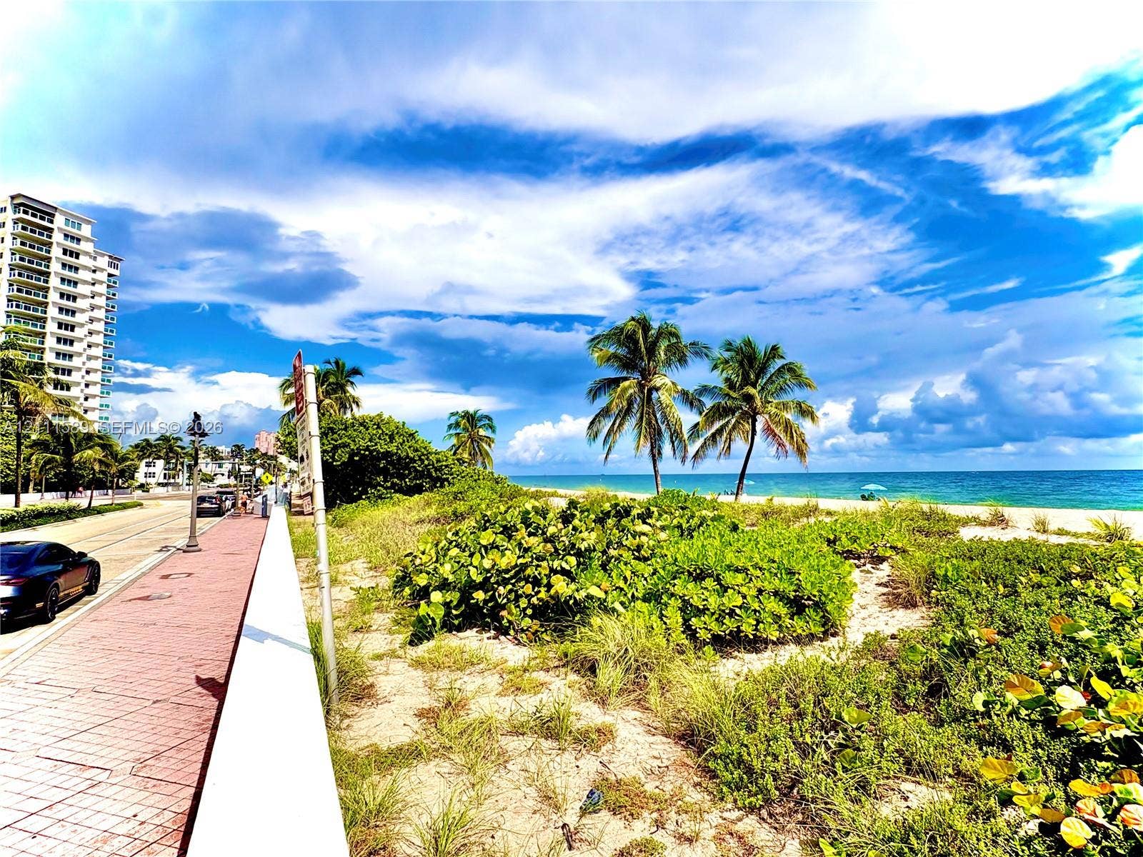 Coastal property featuring a brick-paved sidewalk, decorative street lamps, mature palm trees, native beach vegetation, and direct oceanfront access