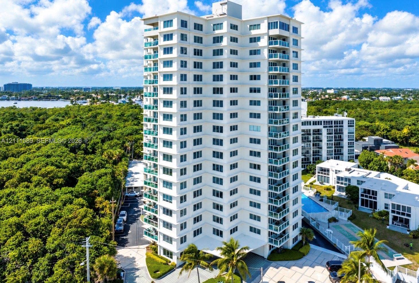 High-rise residential tower featuring private balconies, an exterior swimming pool, multi-level structural design, and paved surface parking