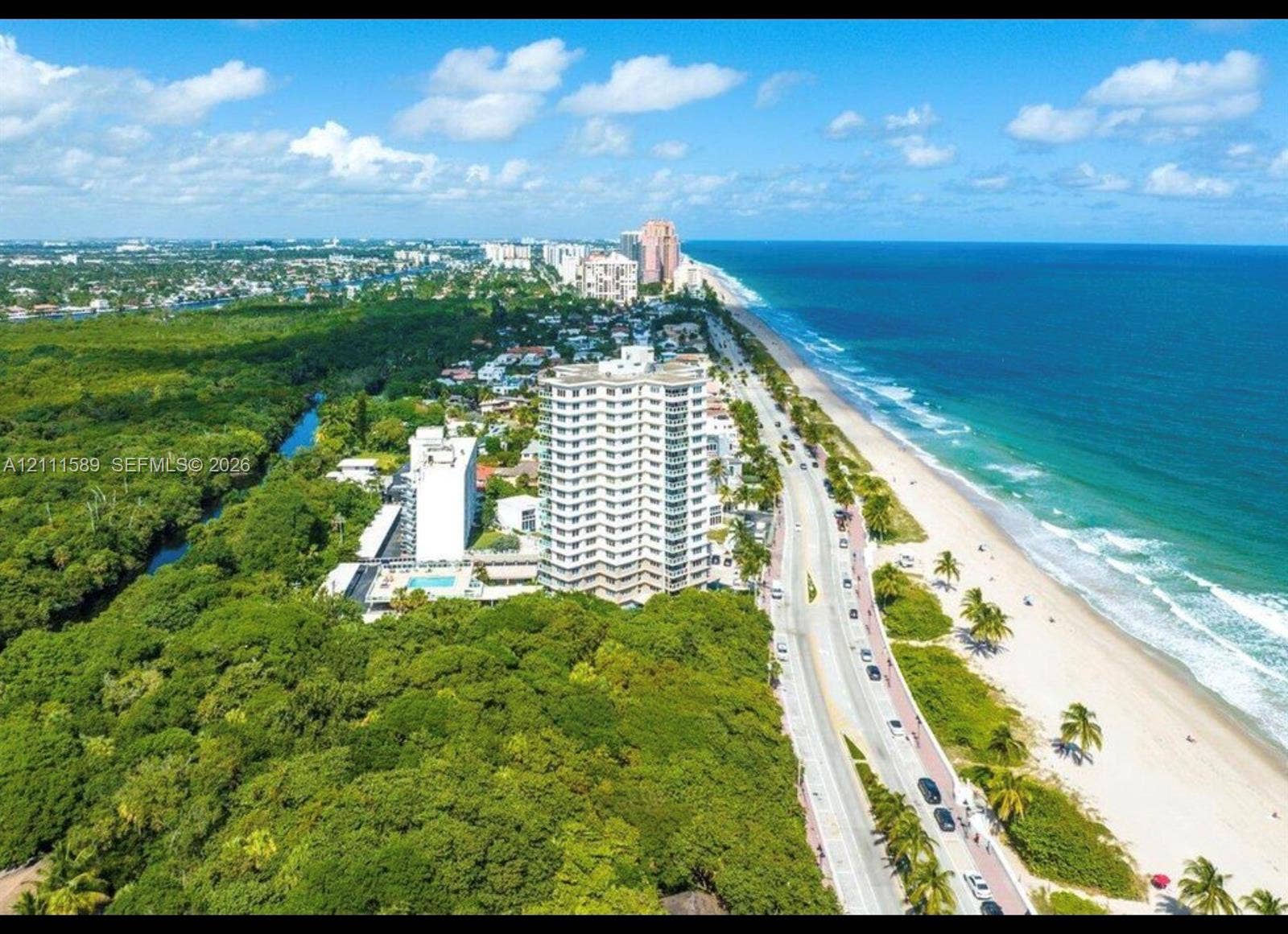 Aerial perspective of coastal residential tower featuring direct shoreline exposure, expansive oceanfront, proximity to wooded preserves, and surrounding high-density corridor