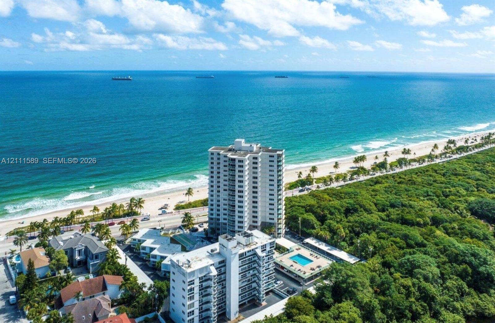Aerial perspective of coastal high-rise buildings featuring a swimming pool, paved sundeck, and proximity to the shoreline