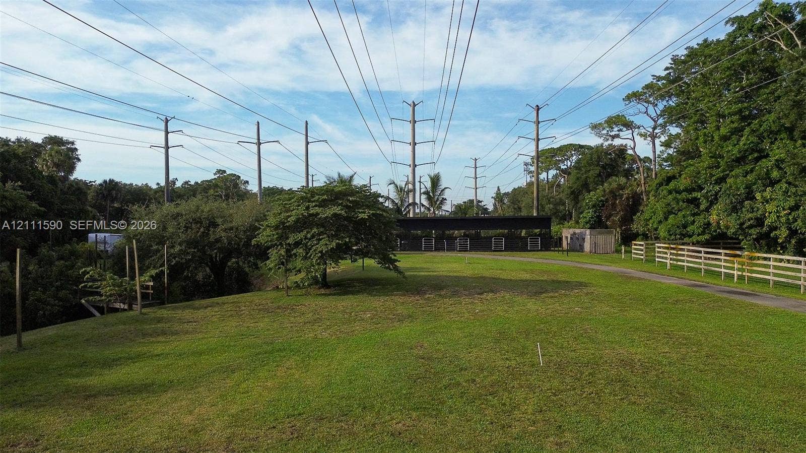 Expansive lot featuring a manicured lawn, mature trees, and white post-and-rail fencing