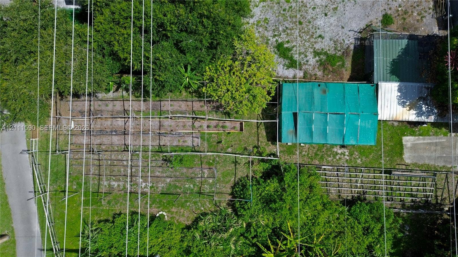 Expansive grounds featuring a series of raised garden beds, a structural shade house with green mesh cover, a slatted wooden trellis system, and mature tree canopy
