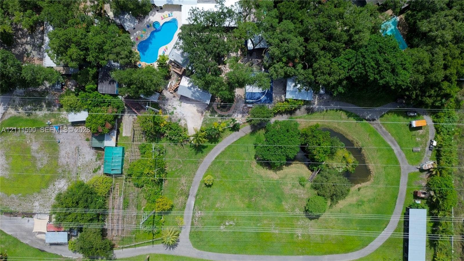Aerial perspective featuring an expansive lot with mature trees, a swimming pool, a pond, and paved pathways