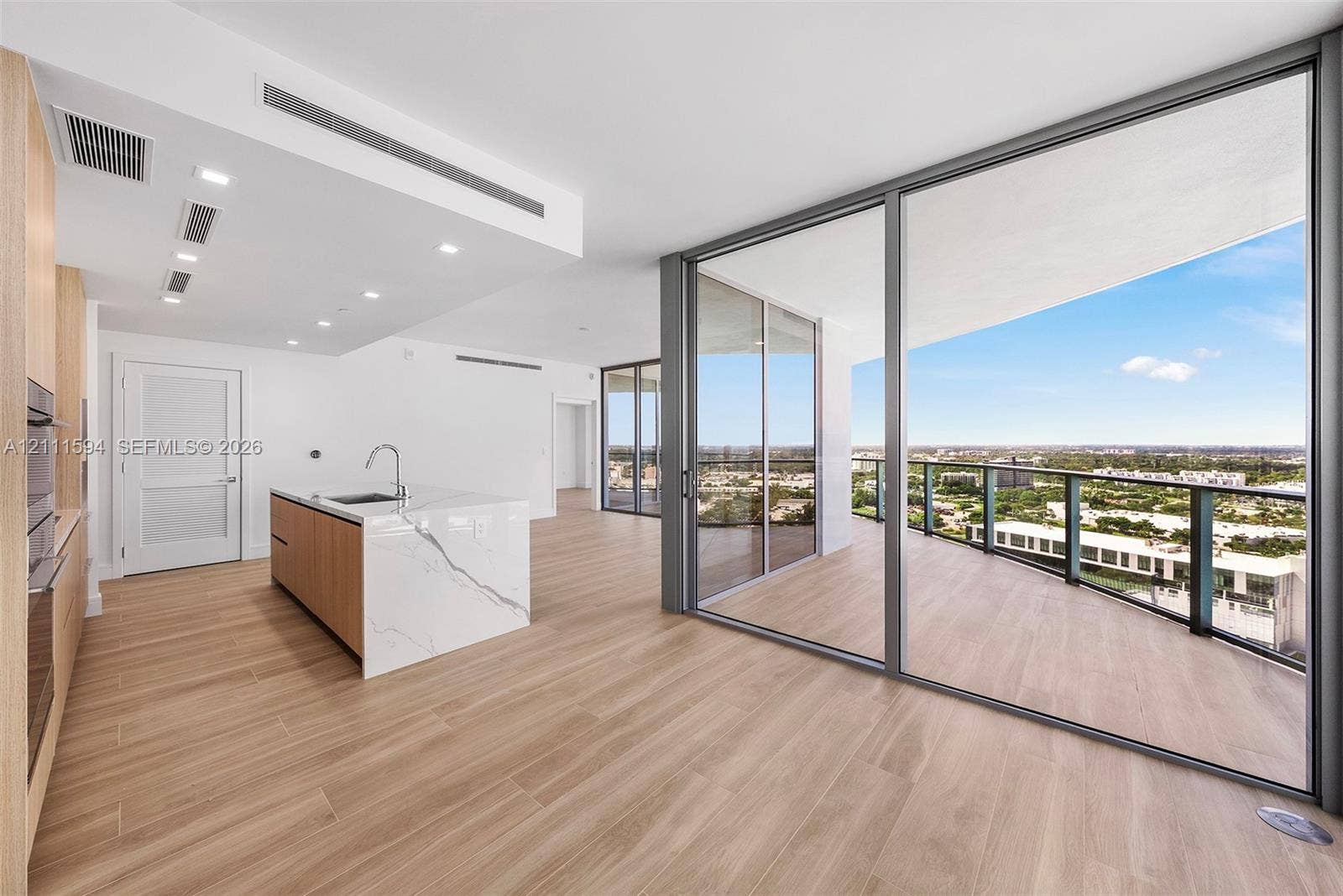 2411 Laguna Circle, #2506, North Miami, FL 33181 Kitchen island with a stone-finish waterfall edge and integrated sink, floor-to-ceiling glass sliding doors, expansive covered balcony, and wood-finish flooring throughout