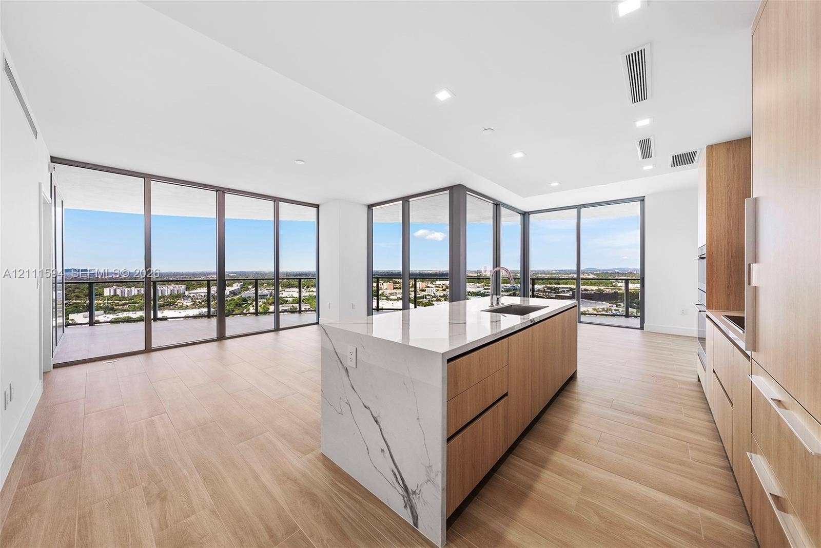 2411 Laguna Circle, #2506, North Miami, FL 33181 Kitchen featuring wood-finish cabinetry, an island with a stone-surface countertop, floor-to-ceiling glass panel walls, and wood-finish flooring