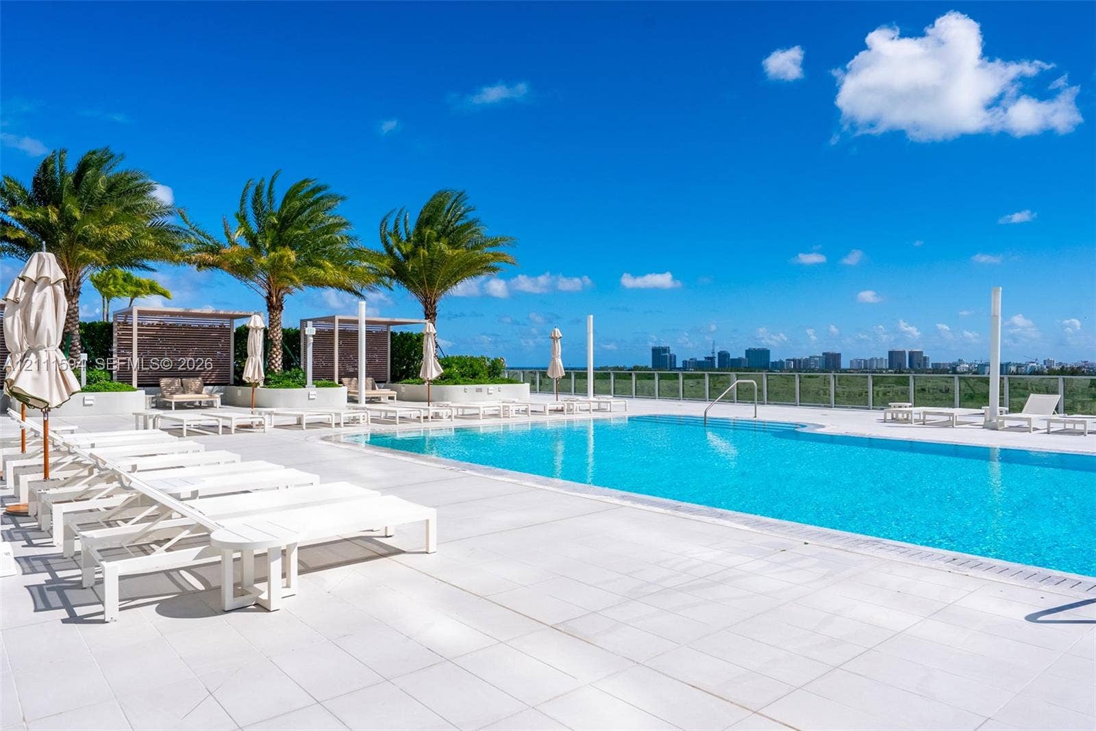 2411 Laguna Circle, #2506, North Miami, FL 33181 Rooftop pool deck featuring stone tile flooring, perimeter glass railings, built-in cabanas, and mature palm trees
