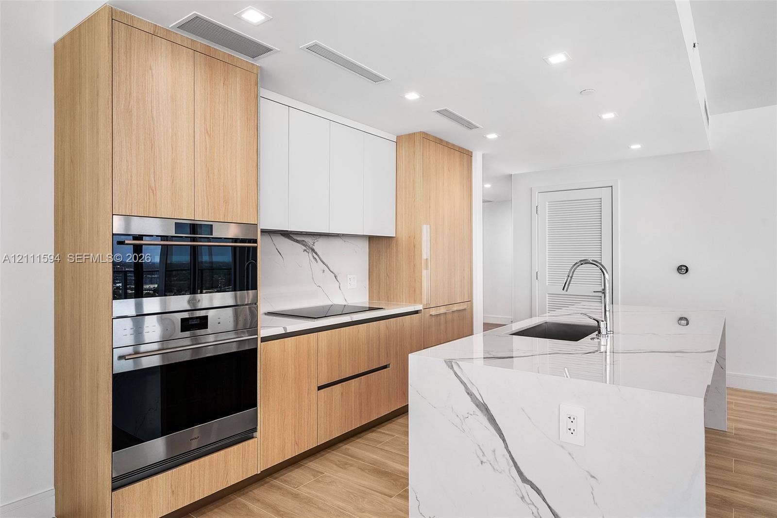 2411 Laguna Circle, #2506, North Miami, FL 33181 Kitchen featuring wood-finish cabinetry, white slab-style upper cabinets, stone-surfaced island with waterfall edge, integrated stainless steel oven and microwave, and recessed ceiling lighting