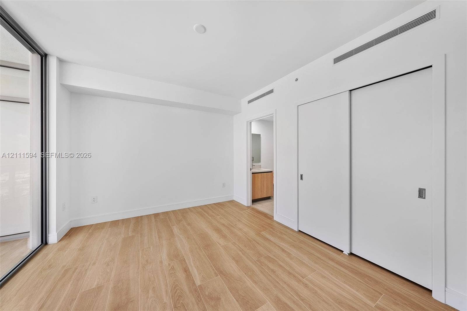 2411 Laguna Circle, #2506, North Miami, FL 33181 Room featuring wood-finish flooring, full-height sliding door closet, floor-to-ceiling glass wall, and smooth-finish white walls