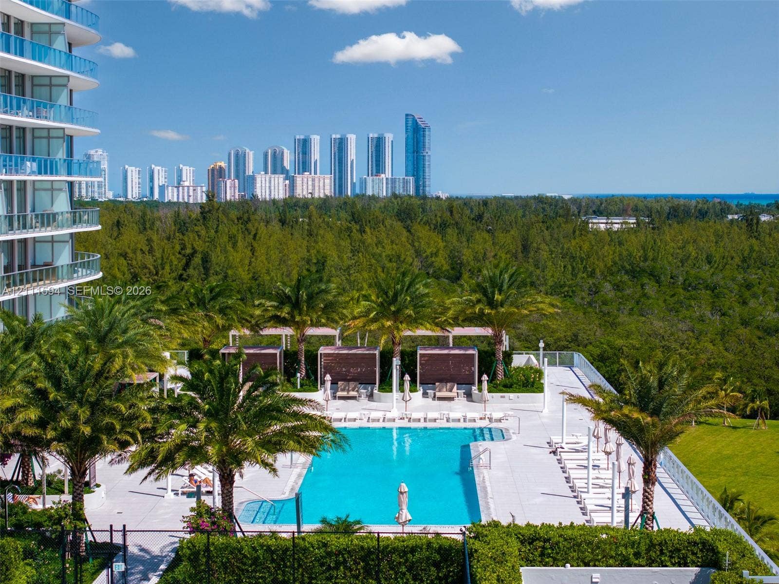 2411 Laguna Circle, #2506, North Miami, FL 33181 Swimming pool with concrete decking, perimeter privacy hedging, mature palm trees, and elevated cabanas