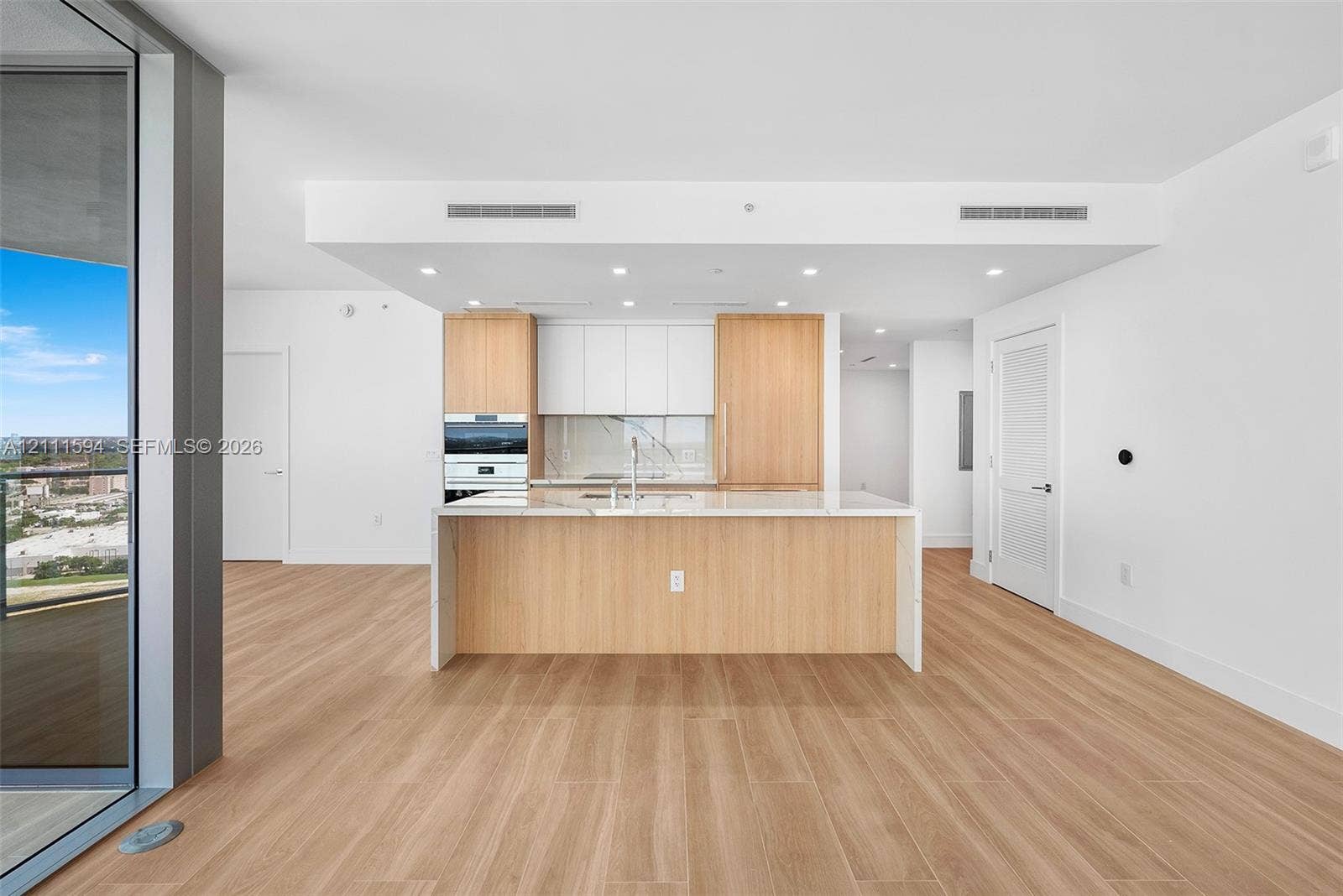 2411 Laguna Circle, #2506, North Miami, FL 33181 Kitchen featuring wood-finish cabinetry, white slab countertops, a central island, recessed lighting, and integrated wall oven