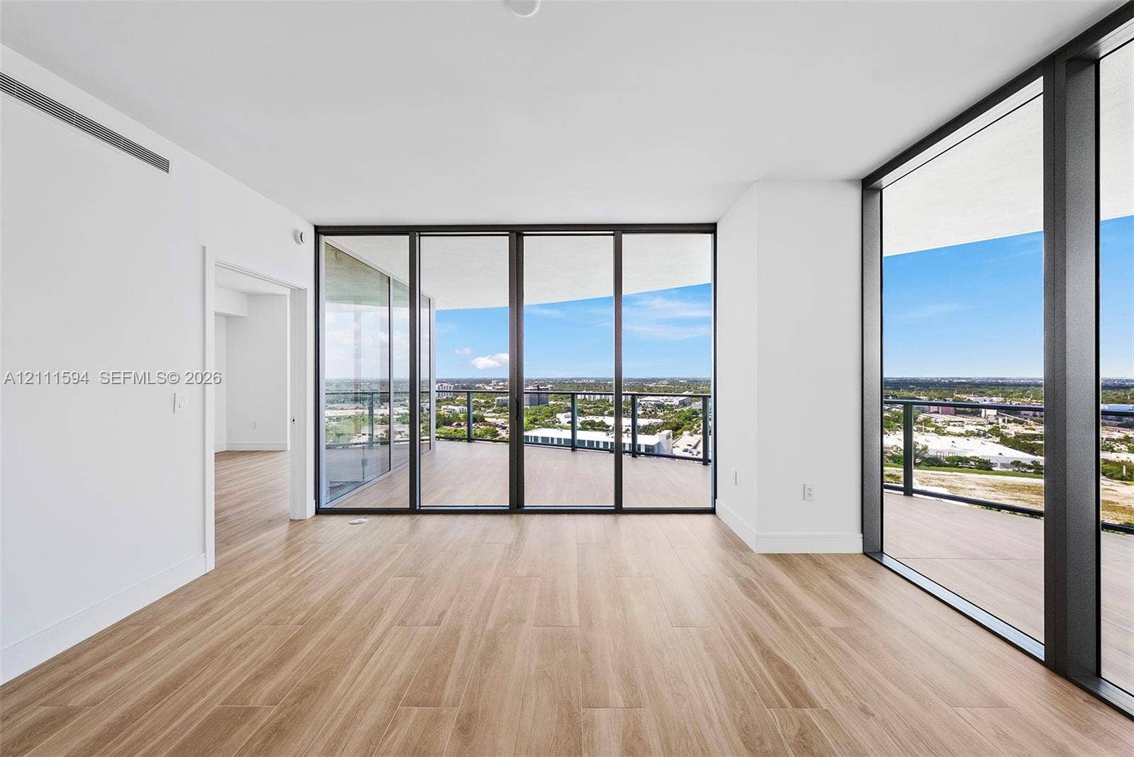 2411 Laguna Circle, #2506, North Miami, FL 33181 Floor-to-ceiling glass sliding doors, expansive wraparound terrace, wood-finish flooring, and minimalist white interior walls