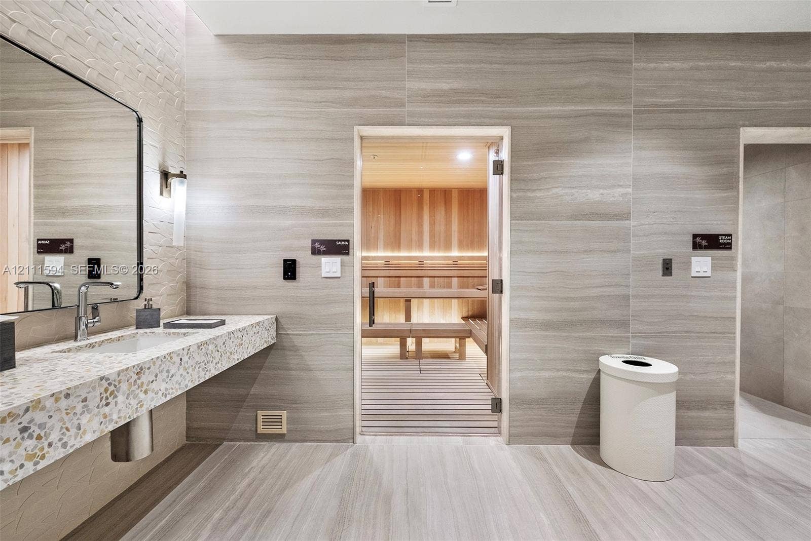 2411 Laguna Circle, #2506, North Miami, FL 33181 Sauna room featuring cedar wood wall paneling and tiered bench seating, complemented by a stone-tiled accent wall, a floating vanity with a terrazzo-style countertop, and a large wall-mounted mirror