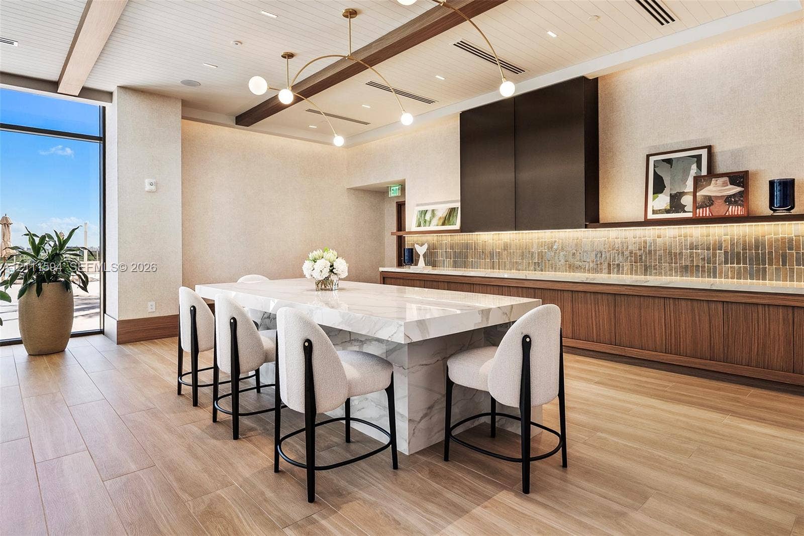 2411 Laguna Circle, #2506, North Miami, FL 33181 Waterfall-edge stone island with bar seating, custom wood-finish cabinetry, linear tile backsplash, wood-finish flooring, and recessed ceiling beams