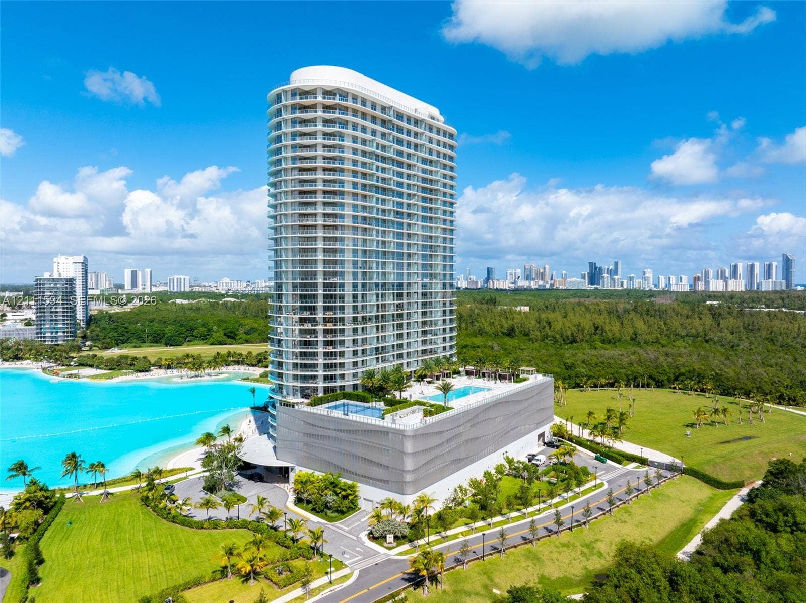 2411 Laguna Circle, #2506, North Miami, FL 33181 High-rise building featuring a glass facade, multiple wraparound balconies, an elevated swimming pool, and curated landscape grounds