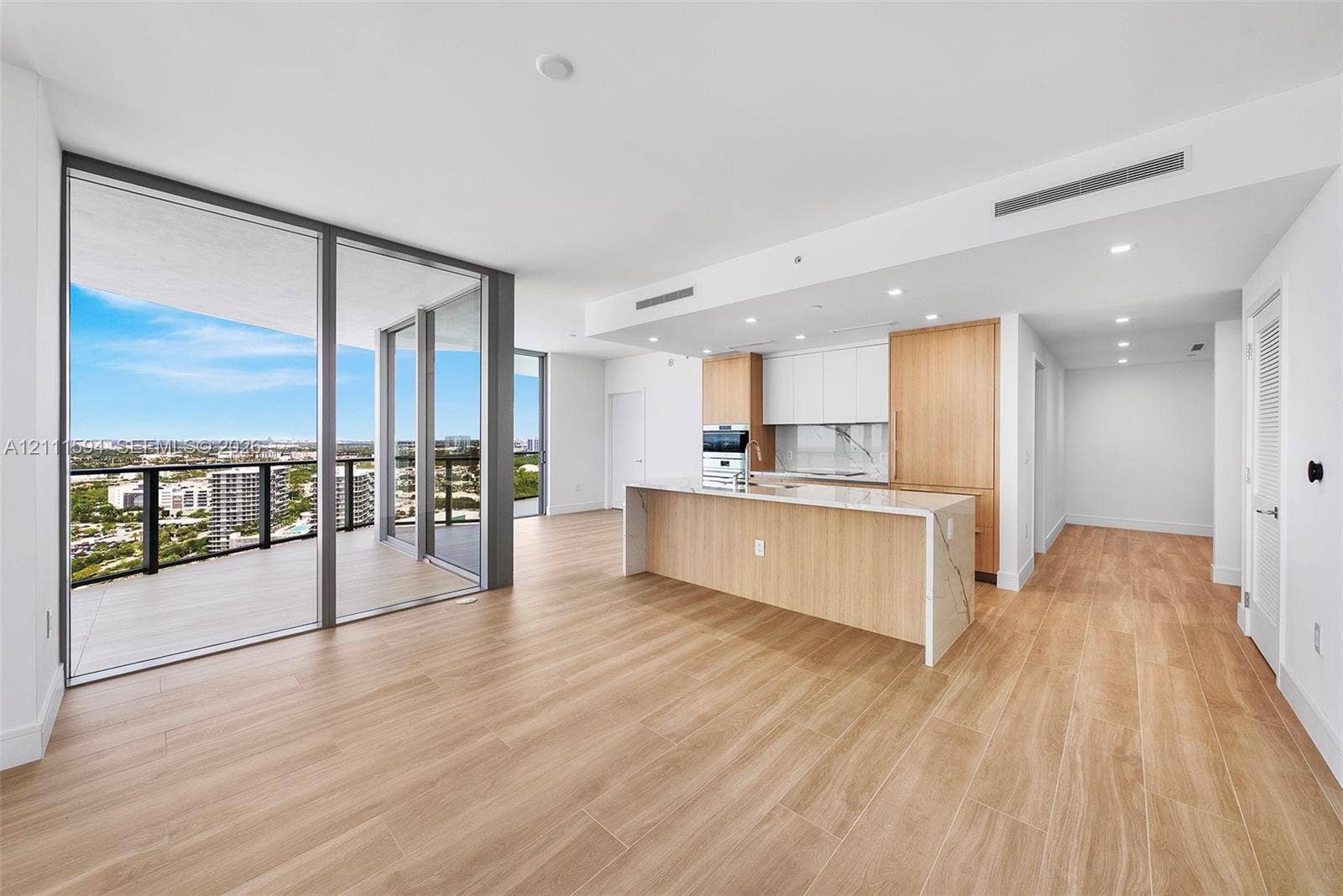 2411 Laguna Circle, #2506, North Miami, FL 33181 Open-concept interior featuring wood-finish flooring, floor-to-ceiling glass panel walls, a wraparound balcony, a kitchen island with stone-finish countertops, and minimalist flat-panel cabinetry