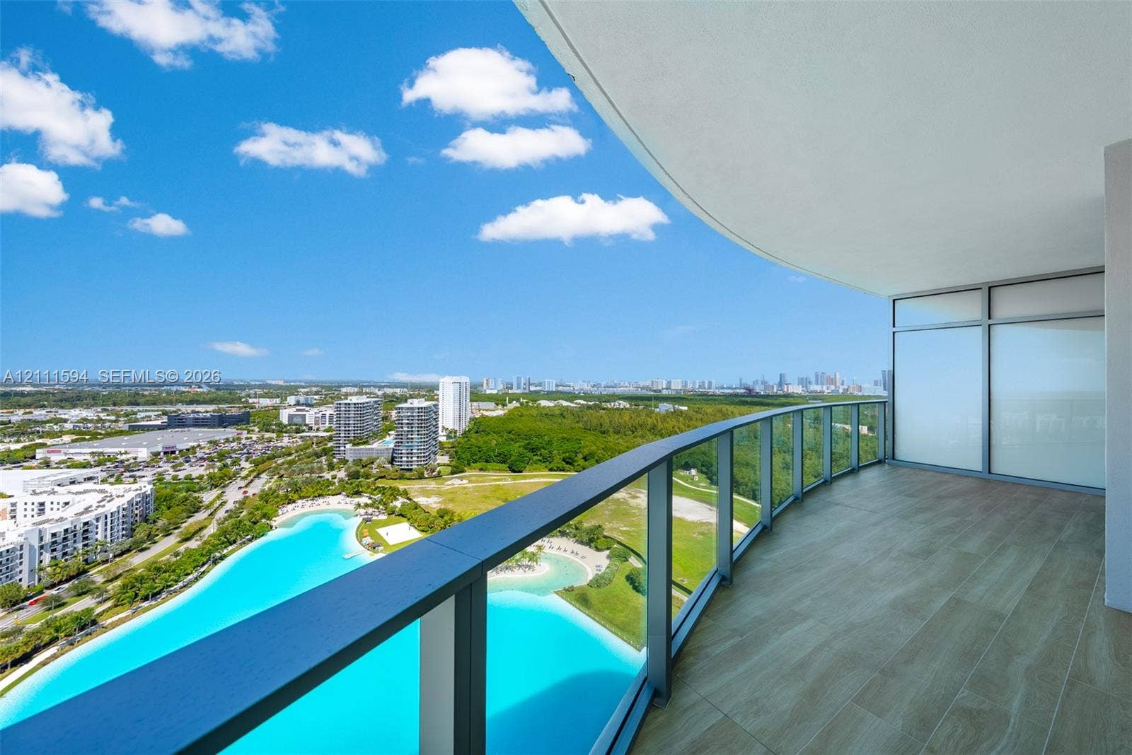 2411 Laguna Circle, #2506, North Miami, FL 33181 Curved balcony featuring wood-finish tile flooring, glass railings, and expansive architectural overhang