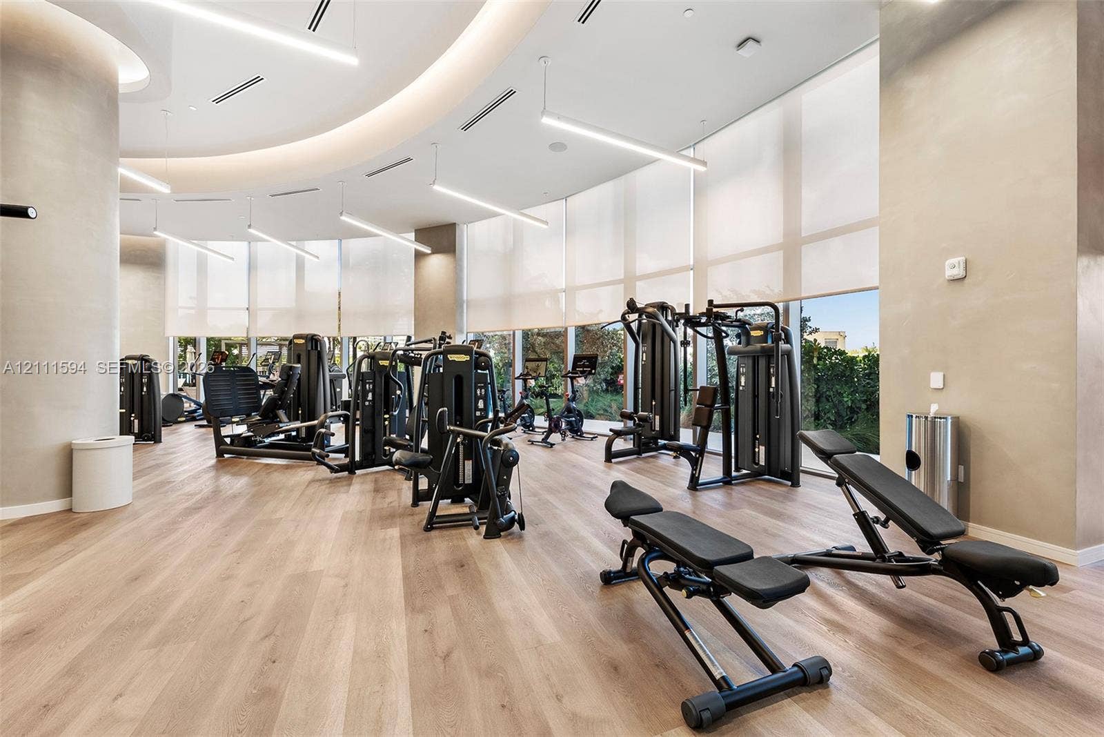 2411 Laguna Circle, #2506, North Miami, FL 33181 Fitness center featuring wood-finish flooring, floor-to-ceiling windows with roller shades, recessed cove lighting, and suspended linear LED fixtures